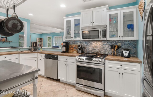 kitchen with tasteful backsplash, white cabinetry, appliances with stainless steel finishes, and butcher block counters