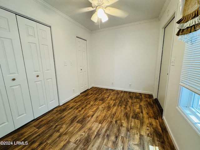 unfurnished bedroom featuring multiple closets, ornamental molding, dark wood-type flooring, and ceiling fan