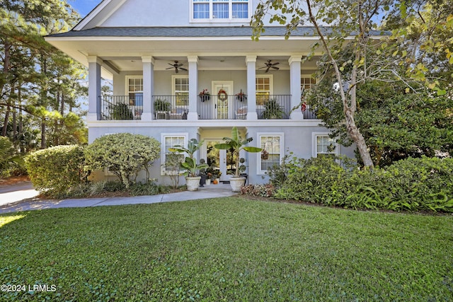 view of front facade with a balcony, a front yard, and ceiling fan