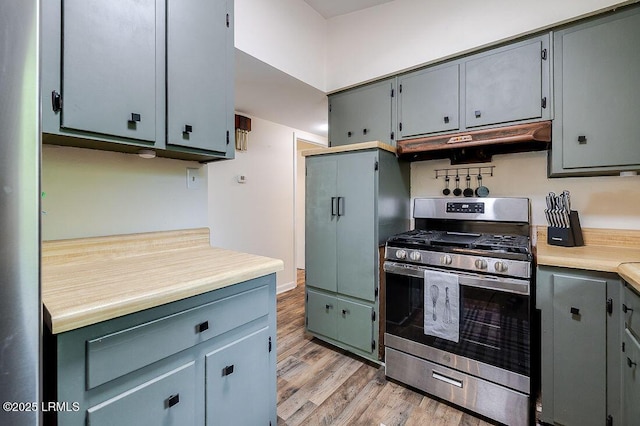 kitchen with stainless steel gas range oven, under cabinet range hood, light wood-style flooring, light countertops, and gray cabinets