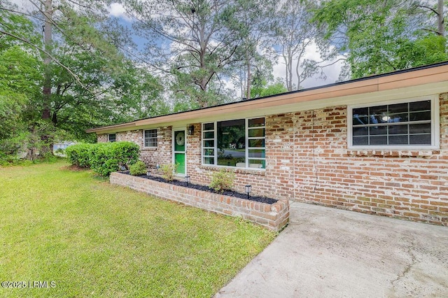 single story home featuring a front lawn, brick siding, and a patio area