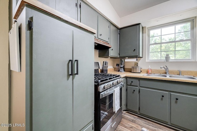 kitchen featuring stainless steel gas range, a sink, gray cabinetry, under cabinet range hood, and freestanding refrigerator