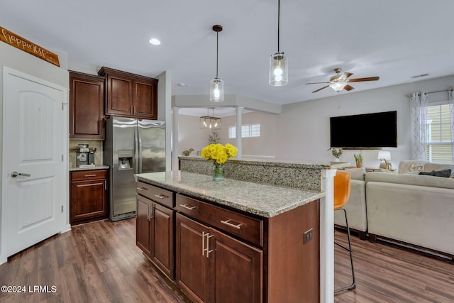 kitchen featuring decorative light fixtures, dark hardwood / wood-style flooring, stainless steel fridge, a kitchen island, and light stone countertops