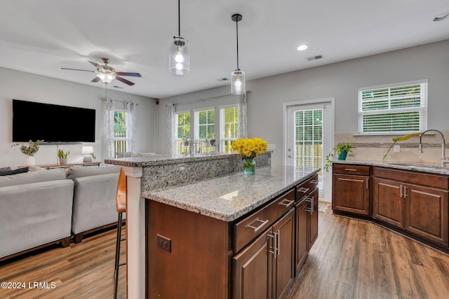 kitchen with sink, hardwood / wood-style flooring, a breakfast bar area, light stone countertops, and decorative light fixtures