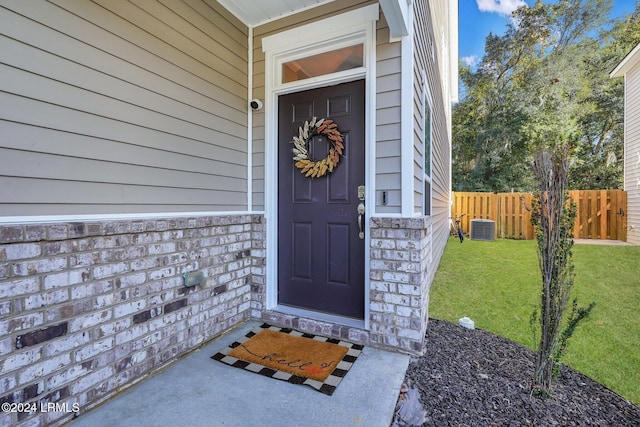 view of exterior entry featuring central AC and a yard