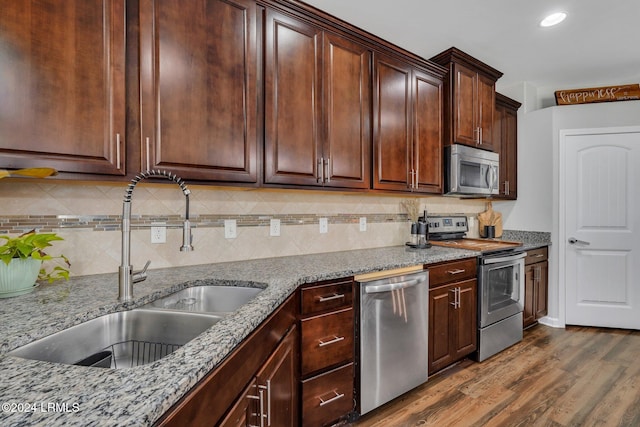 kitchen with sink, dark brown cabinets, stainless steel appliances, light stone countertops, and dark hardwood / wood-style flooring