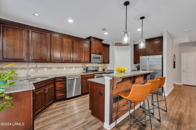 kitchen featuring sink, light stone counters, a center island, hanging light fixtures, and stainless steel appliances