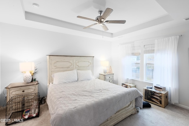 bedroom with light colored carpet, a raised ceiling, and ceiling fan