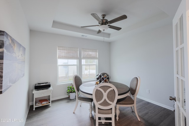 dining area featuring dark hardwood / wood-style flooring, a tray ceiling, and ceiling fan