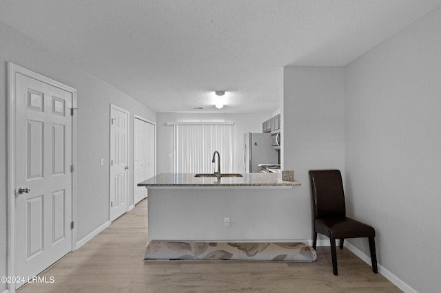 kitchen featuring appliances with stainless steel finishes, sink, kitchen peninsula, light stone countertops, and light hardwood / wood-style flooring