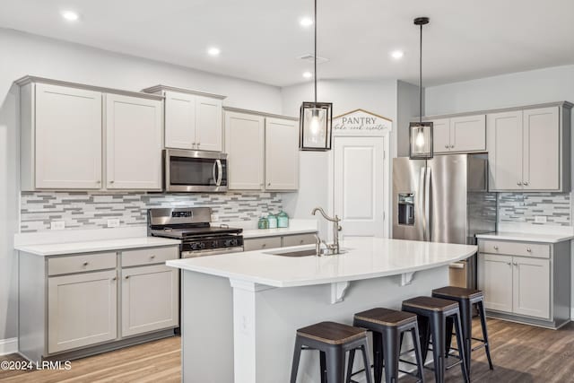 kitchen featuring sink, gray cabinets, appliances with stainless steel finishes, a kitchen island with sink, and hanging light fixtures