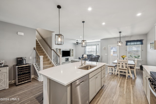 kitchen with pendant lighting, sink, beverage cooler, a kitchen island with sink, and stainless steel dishwasher