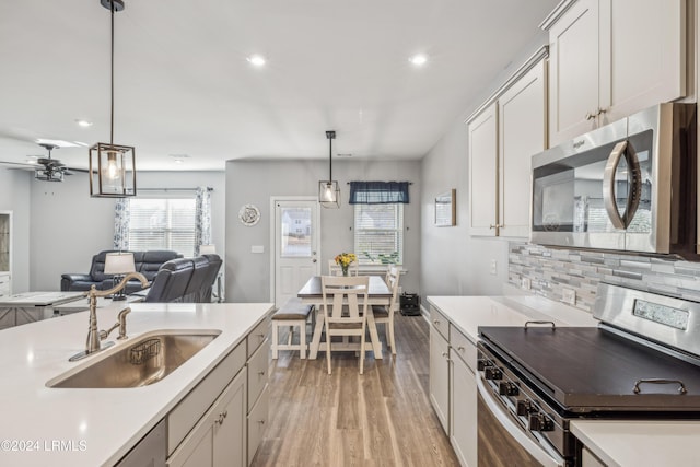 kitchen featuring sink, tasteful backsplash, white cabinetry, decorative light fixtures, and appliances with stainless steel finishes