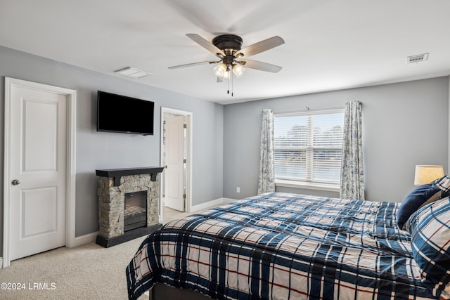 carpeted bedroom with a stone fireplace and ceiling fan