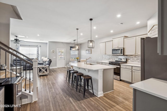 kitchen with sink, a breakfast bar area, hanging light fixtures, stainless steel appliances, and an island with sink