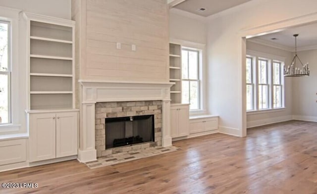 unfurnished living room featuring ornamental molding, a wealth of natural light, an inviting chandelier, and light hardwood / wood-style floors