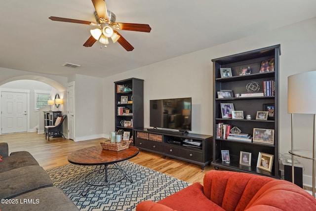 living area with arched walkways, visible vents, ceiling fan, and wood finished floors