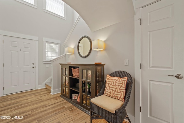 sitting room featuring a towering ceiling, light wood-style floors, stairs, and baseboards