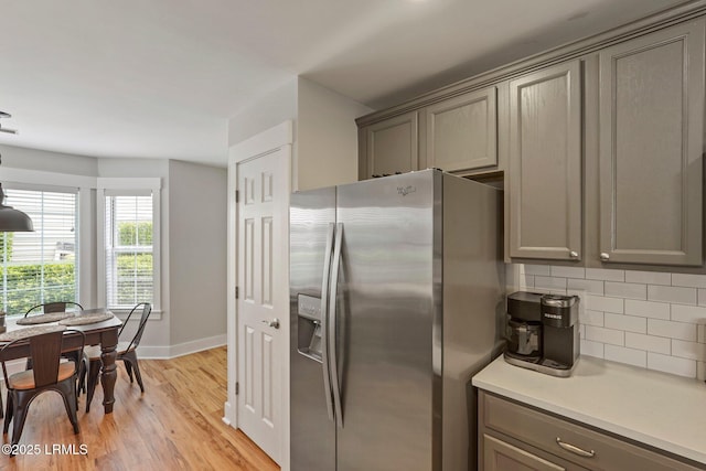 kitchen with gray cabinetry, stainless steel refrigerator with ice dispenser, backsplash, and light wood finished floors