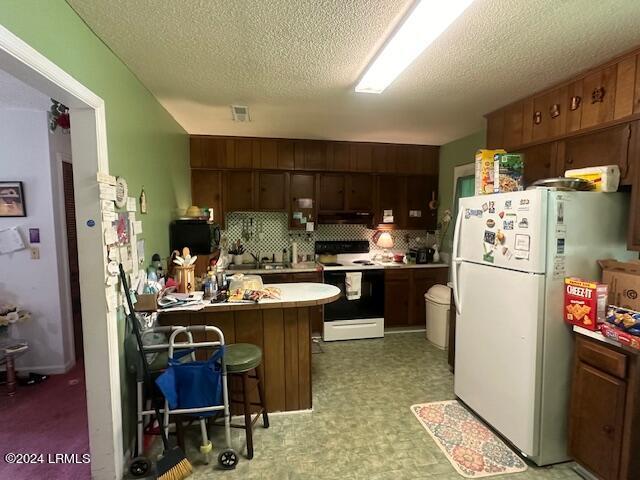 kitchen featuring white appliances, a breakfast bar area, decorative backsplash, and a textured ceiling