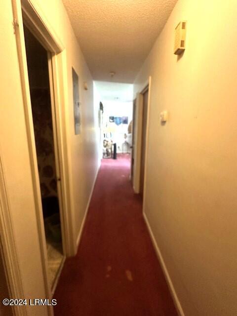 corridor with a textured ceiling and dark colored carpet