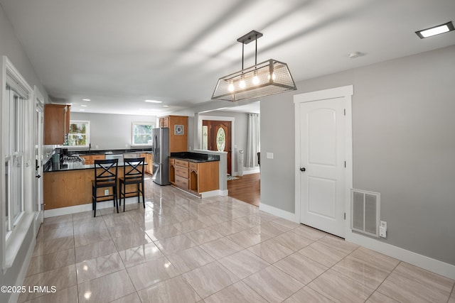 702 Center Dr W, Beaufort, SC 29902 - kitchen with freestanding refrigerator, brown cabinetry, dark countertops, a peninsula, and a kitchen bar