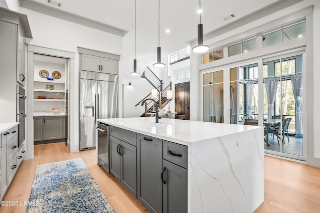 kitchen with a kitchen island, light stone countertops, a sink, gray cabinetry, and stainless steel appliances