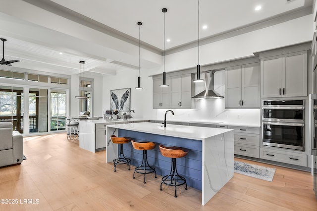 kitchen featuring beam ceiling, a breakfast bar, wall chimney exhaust hood, a sink, and gray cabinetry