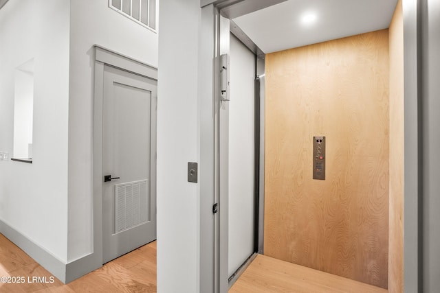hallway featuring visible vents, elevator, and light wood-type flooring
