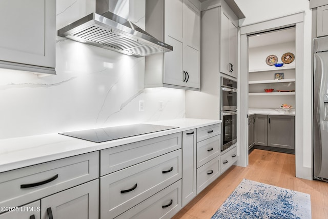 kitchen with wall chimney exhaust hood, appliances with stainless steel finishes, light wood finished floors, and gray cabinetry