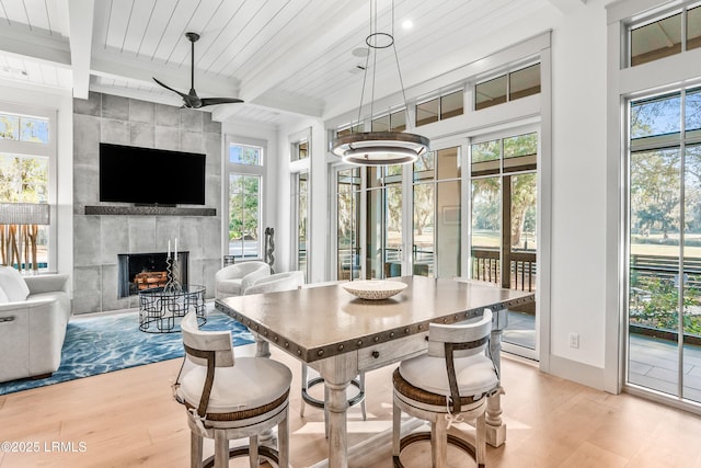 interior space with beamed ceiling, wooden ceiling, a tiled fireplace, a ceiling fan, and light wood finished floors