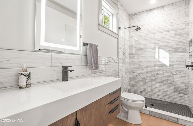 bathroom featuring tile walls, wood finished floors, vanity, toilet, and tiled shower