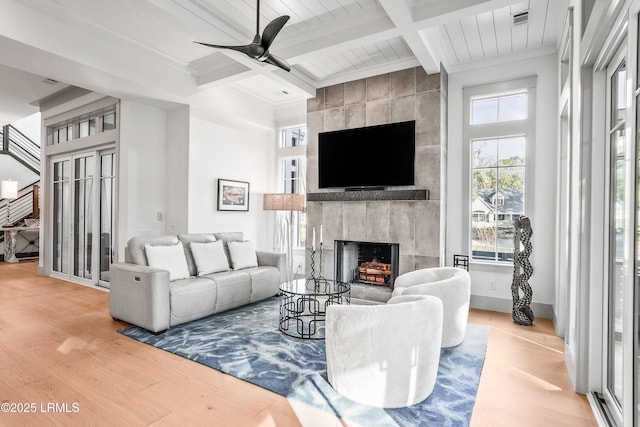 living area with beam ceiling, a fireplace, a ceiling fan, and wood finished floors