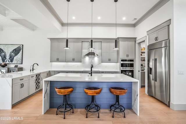 kitchen with gray cabinetry, appliances with stainless steel finishes, light stone countertops, and a sink