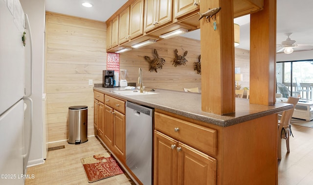 kitchen with wooden walls, sink, white fridge, stainless steel dishwasher, and ceiling fan