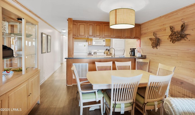 dining space with dark hardwood / wood-style floors, wooden walls, sink, and crown molding