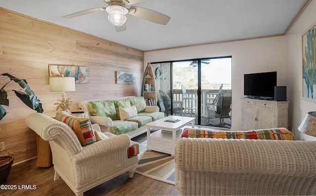 living room featuring hardwood / wood-style floors, wooden walls, ornamental molding, and ceiling fan