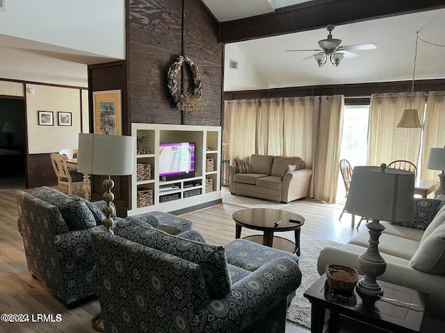 living room featuring hardwood / wood-style flooring, ceiling fan, wooden walls, and vaulted ceiling with beams