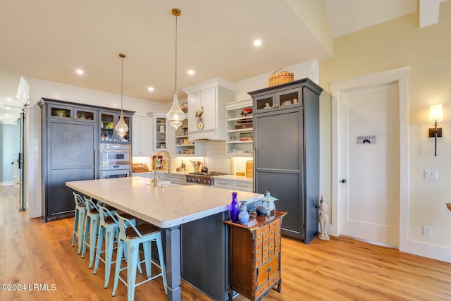 kitchen featuring pendant lighting, a breakfast bar, light stone countertops, and a center island with sink