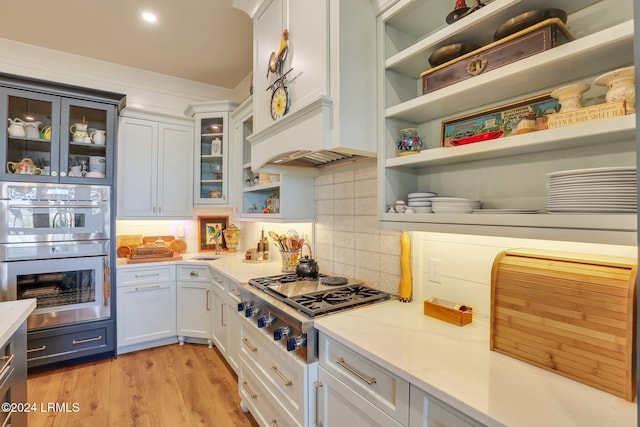 kitchen featuring light hardwood / wood-style flooring, appliances with stainless steel finishes, white cabinetry, backsplash, and light stone countertops