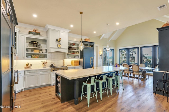 kitchen featuring pendant lighting, white cabinetry, a kitchen breakfast bar, light stone countertops, and an island with sink