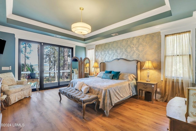 bedroom featuring a raised ceiling, hardwood / wood-style floors, and access to exterior