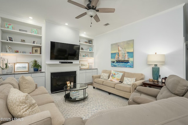 277 Pleasant Point Dr, Beaufort, SC 29907 - living area featuring built in shelves, ornamental molding, a ceiling fan, a glass covered fireplace, and recessed lighting