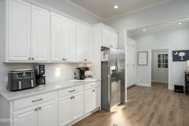 277 Pleasant Point Dr, Beaufort, SC 29907 - kitchen with stainless steel refrigerator with ice dispenser, decorative backsplash, white cabinets, light wood finished floors, and crown molding