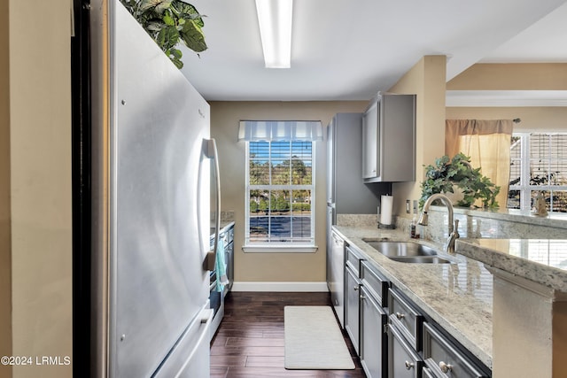 kitchen with sink, appliances with stainless steel finishes, gray cabinetry, light stone countertops, and a healthy amount of sunlight