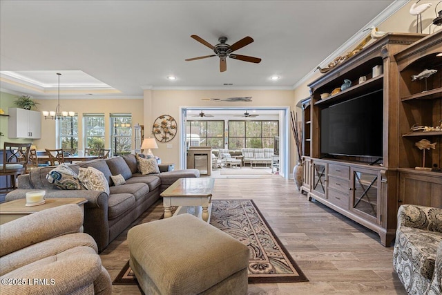 living room with ornamental molding, plenty of natural light, ceiling fan with notable chandelier, and light wood-type flooring