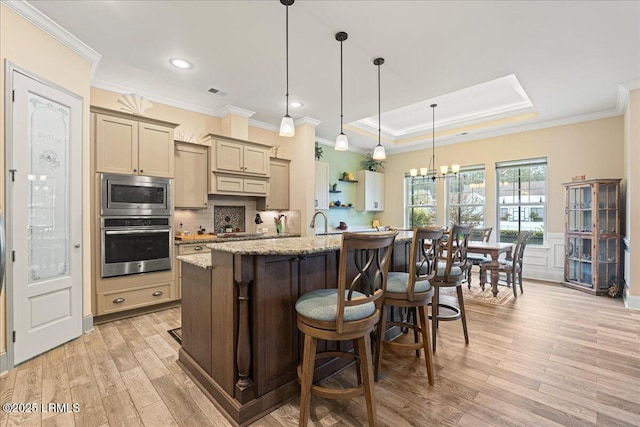 kitchen with appliances with stainless steel finishes, a kitchen breakfast bar, light stone countertops, an island with sink, and light wood-type flooring