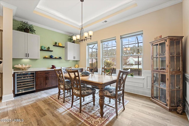 dining space featuring wine cooler, a tray ceiling, crown molding, and light wood-type flooring