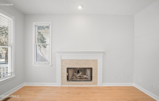 unfurnished living room with a tile fireplace, baseboards, and wood finished floors