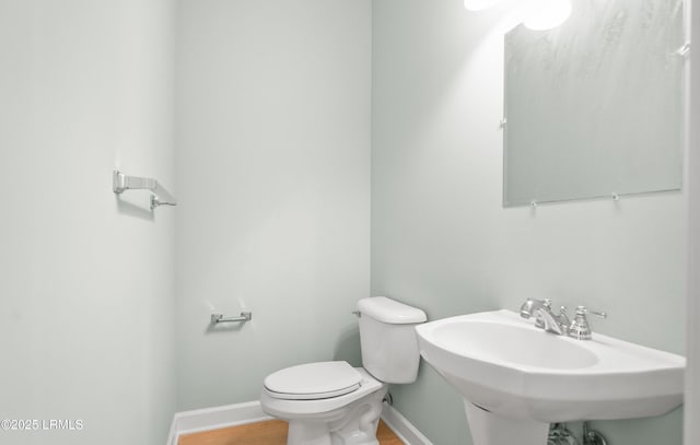 bathroom featuring wood finished floors, toilet, baseboards, and a sink